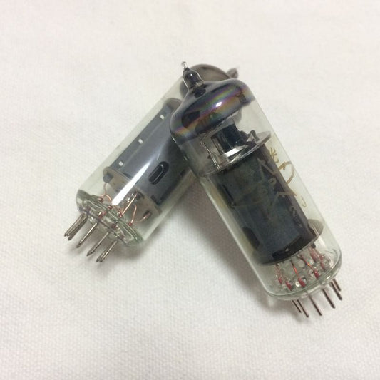 Two vacuum tubes with pins for insertion, one standing upright and the other lying on its side, on a white fabric surface.